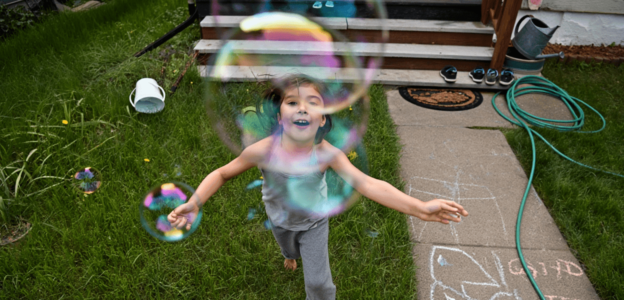 Child joyfully playing with bubbles in a grassy yard.